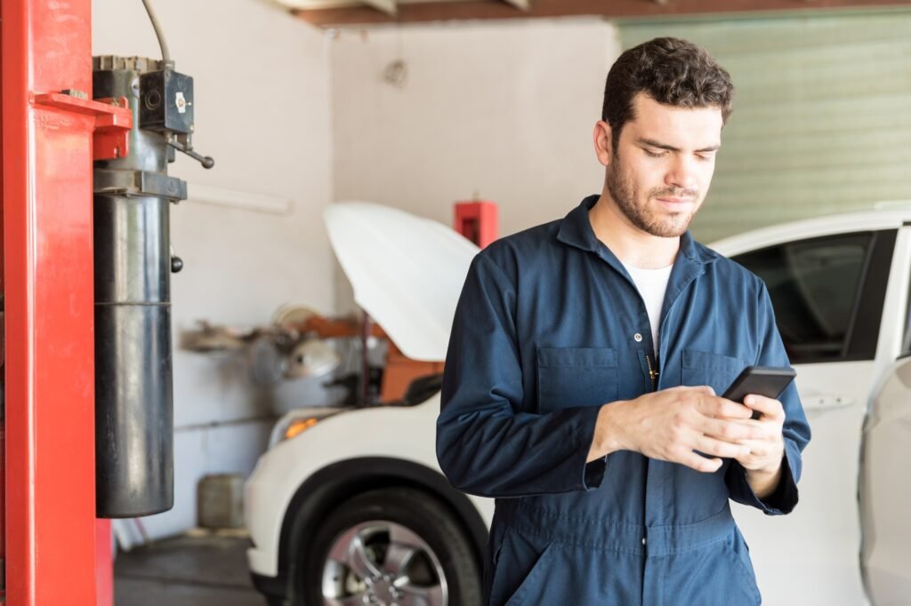 Maintenance Worker Using Mobile Phone In Auto Repair Shop